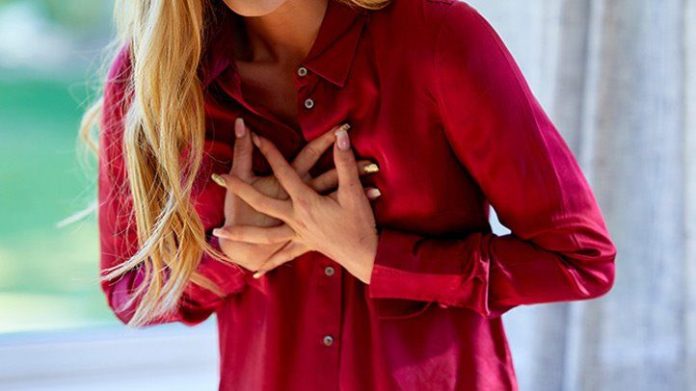 a woman clutching at her heart because of chest pain, a symptom of heart attack